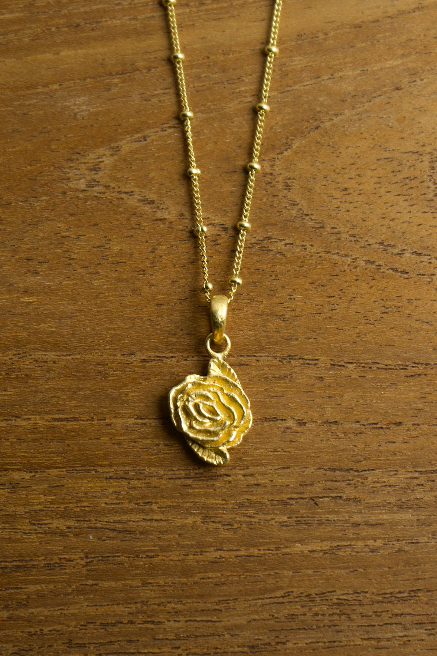 Gold necklace with a rose pendant on a wooden surface