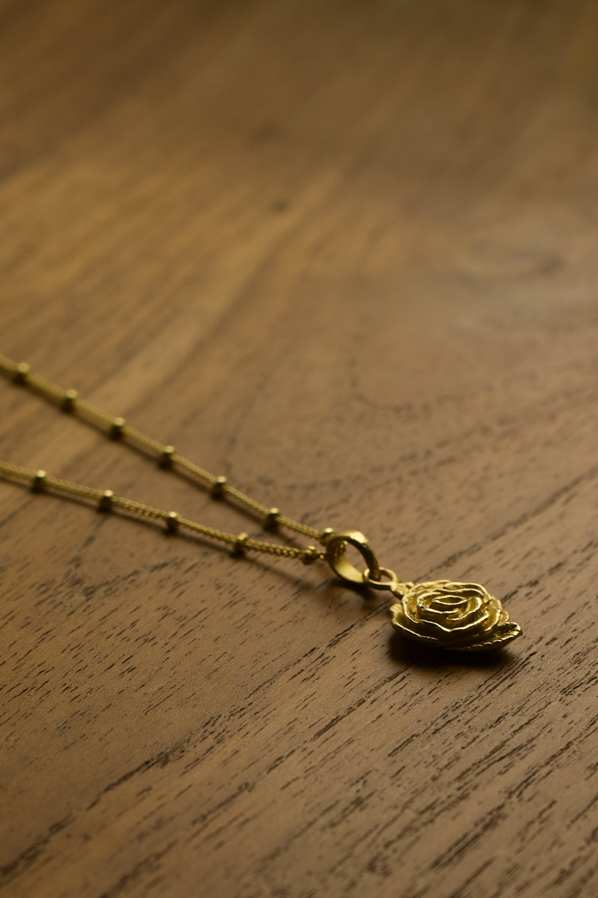Gold necklace with a rose pendant on a wooden surface